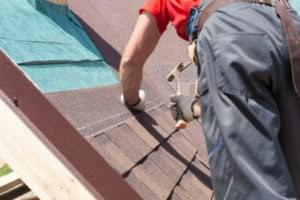 Roofer builder worker use a hammer for installing roofing shingles