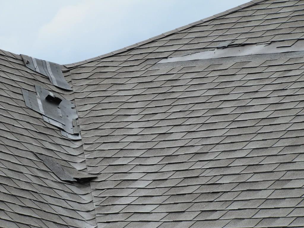 Damaged asphalt roof with missing and torn off shingles.