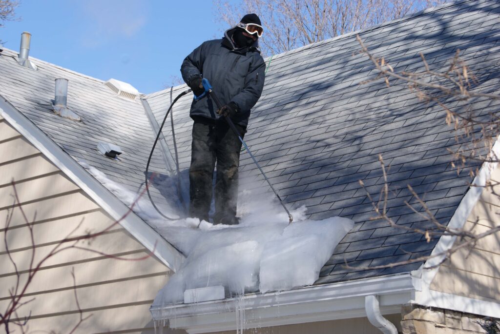 Roofing professional using a steam machine to melt an ice dam.