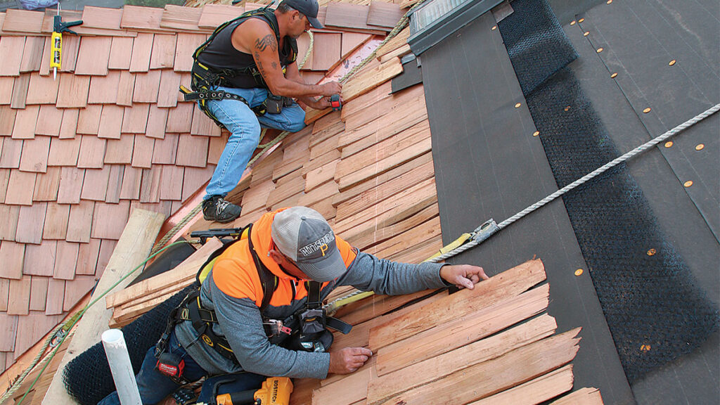 Two contractors installing cedar shake roofing. 