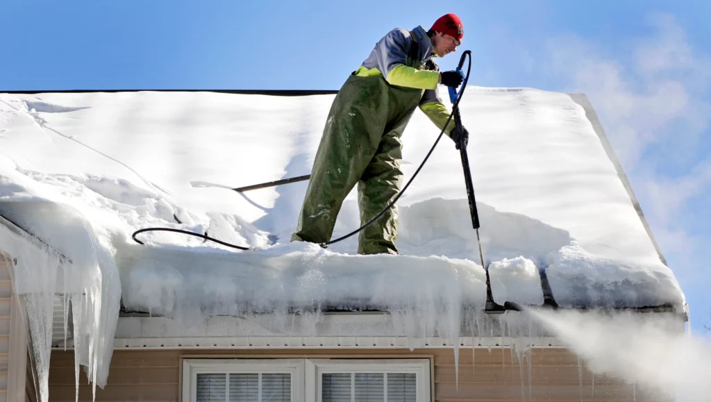 Roofing contractor on a roof, using a steam machine to melt icicles on the gutters.