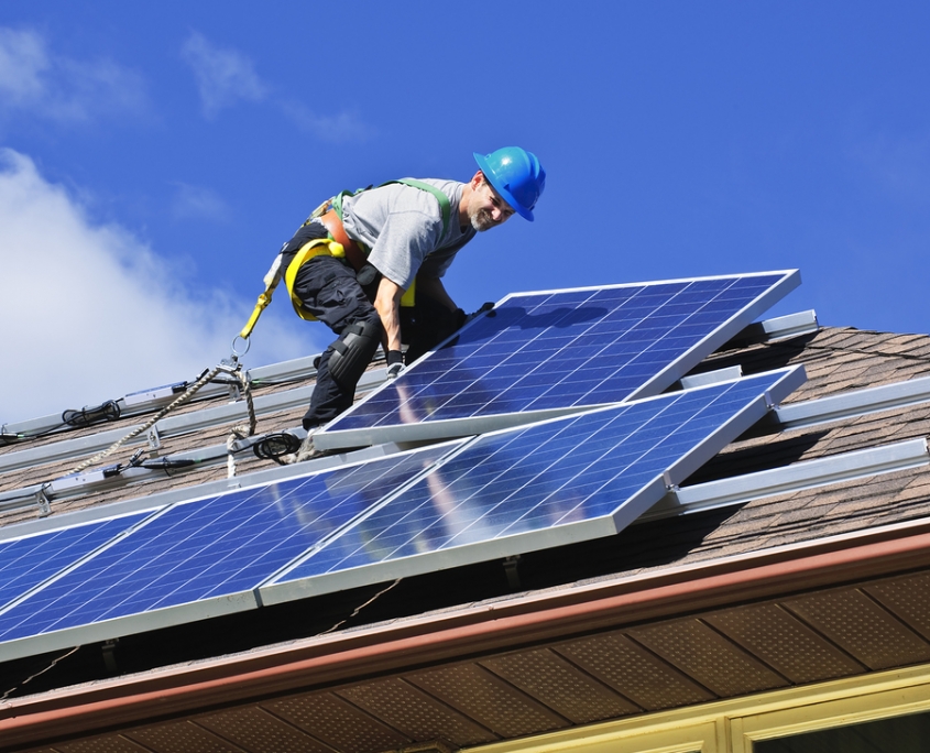 Roofing contractor installing solar panels on an asphalt roof.