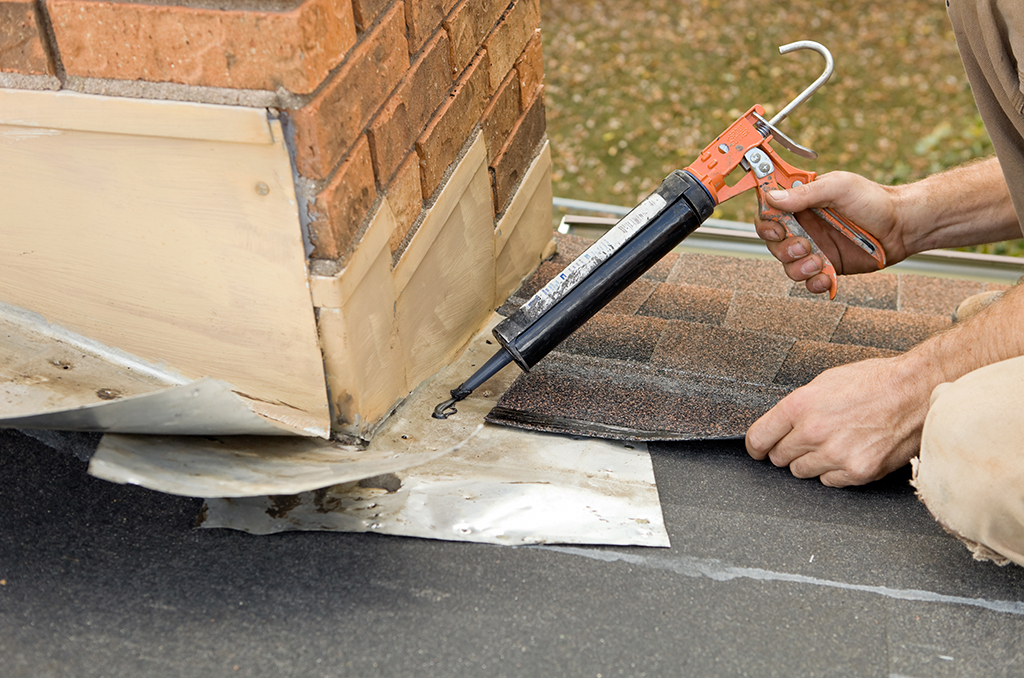 Roofing professional re-caulking roof flashing. 