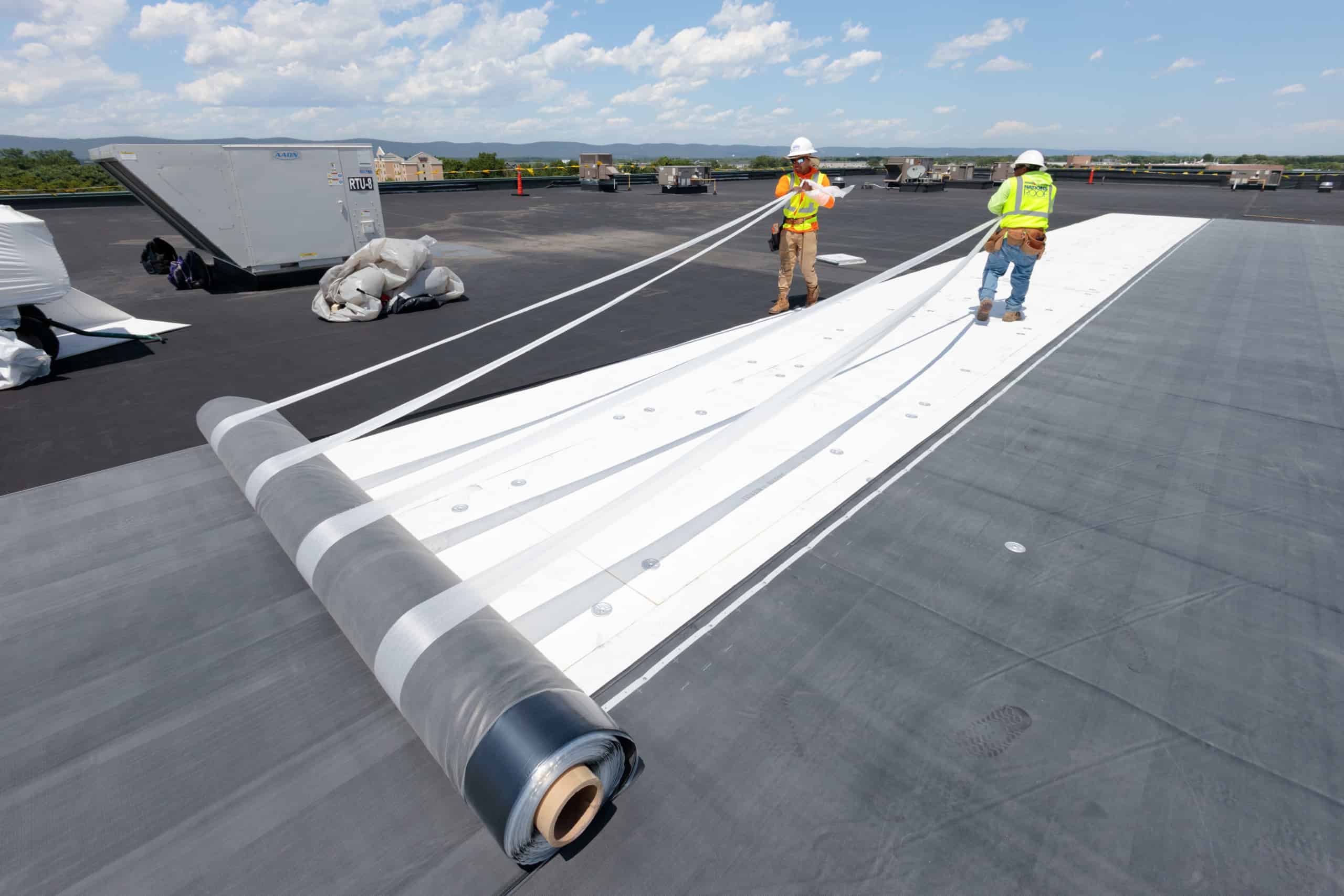 Roofing professionals installing a roll of single-ply roofing membrane.