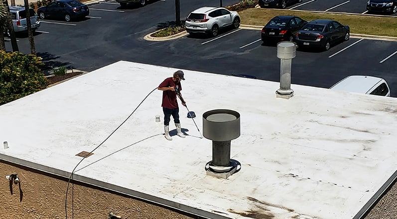 Roofing contractor pressure-washing a flat roof. 