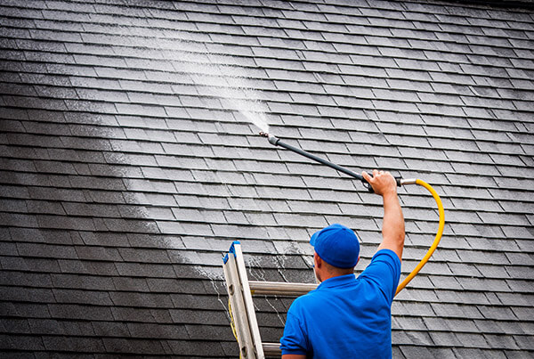 Roofing professional spraying a cleaning solution on an asphalt roof.