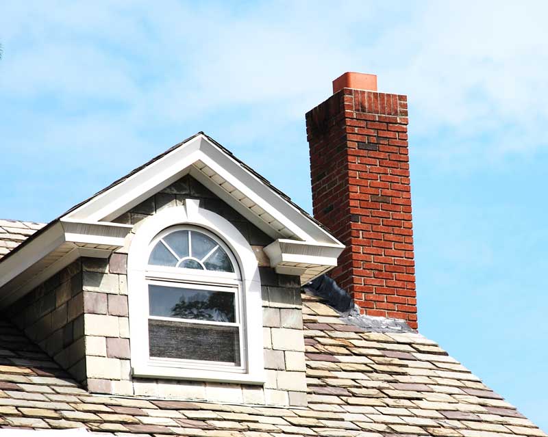 Red brick chimney protruding from a rooftop. 