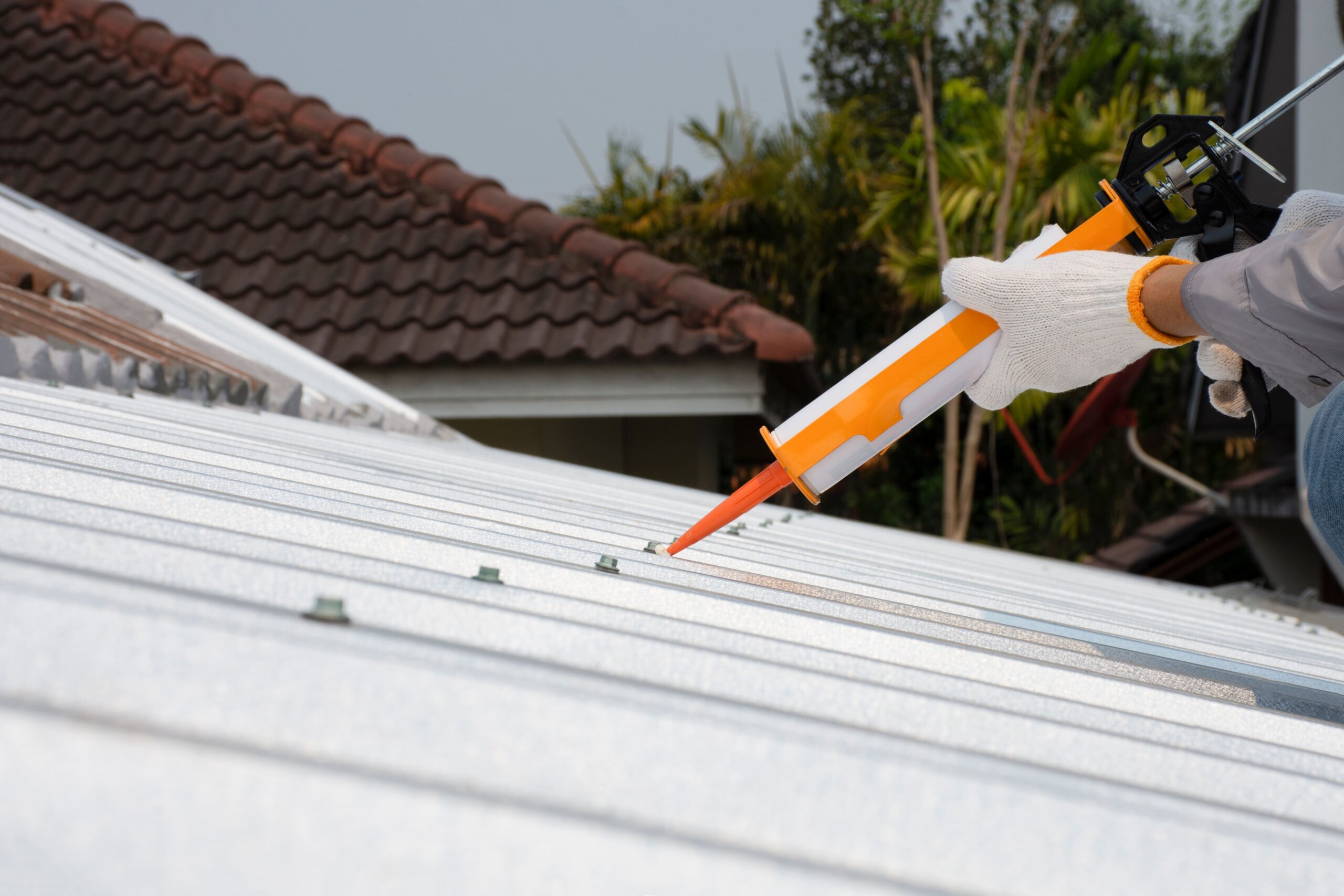 Gloved hand sealing a metal roof with caulk.