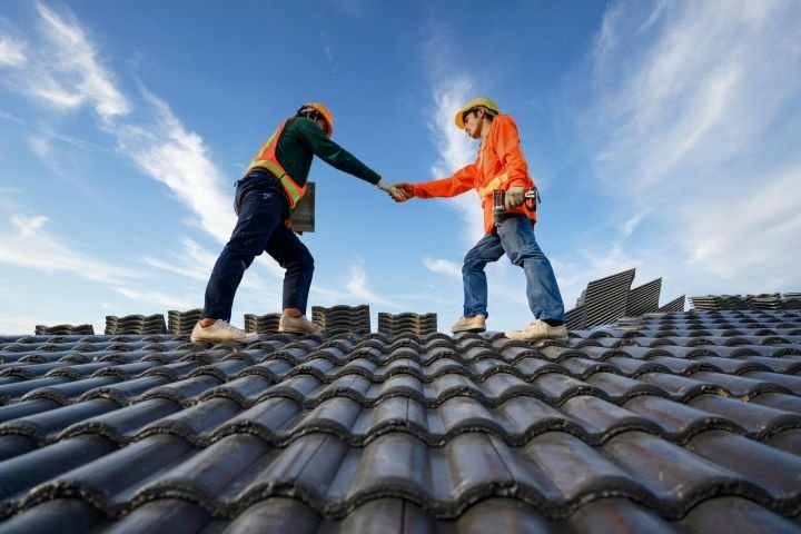 Two roofing contractors shaking hands on top of a metal roof.